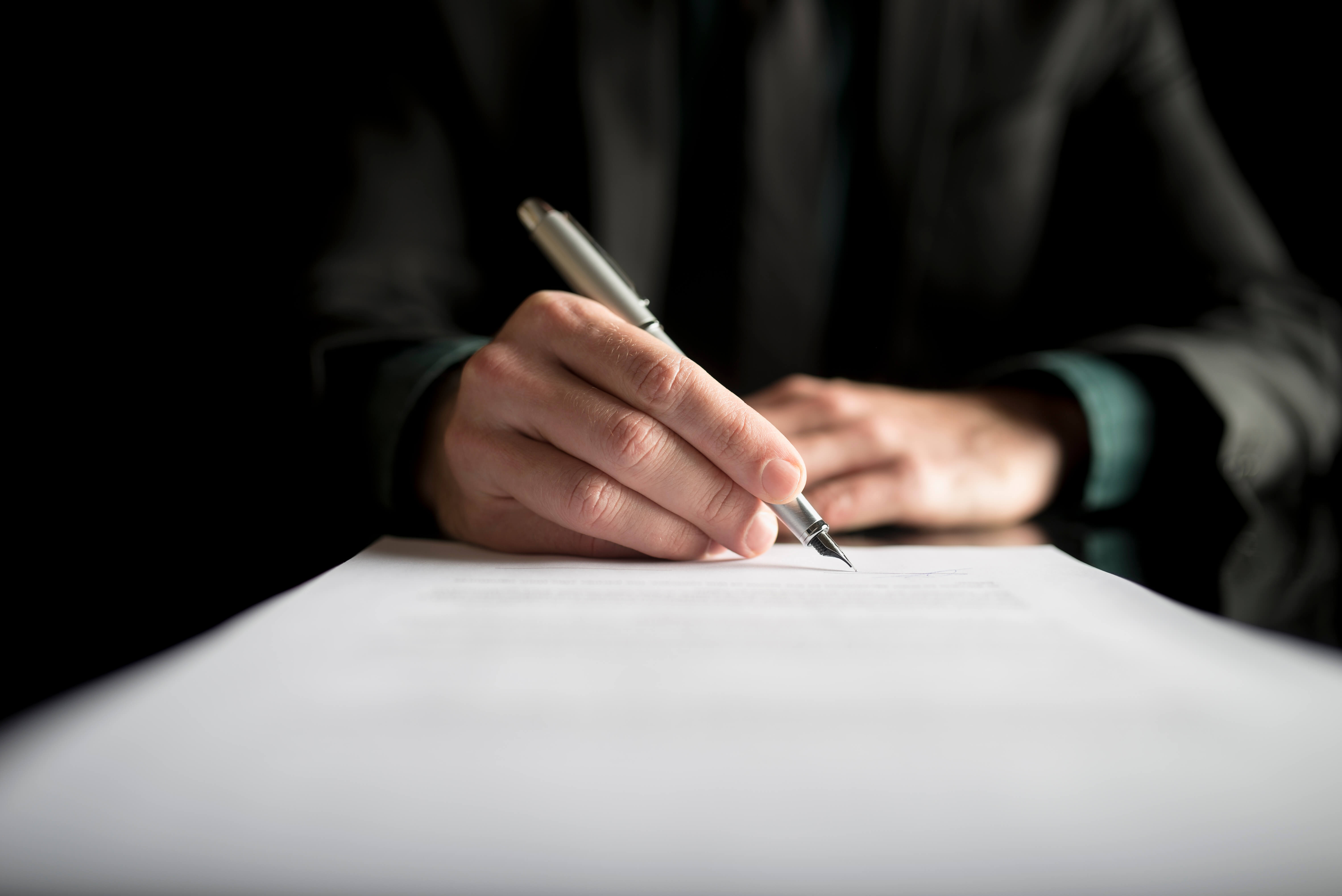 Closeup of senior signing a retirement notice to their employer, placed on black desk.
